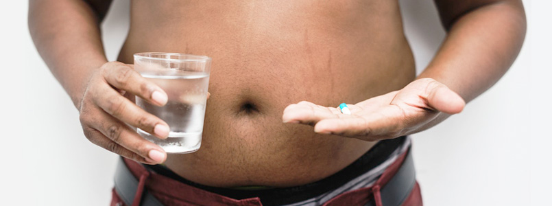 overweight man holding glass of water in one had and Adipex capsules in the other