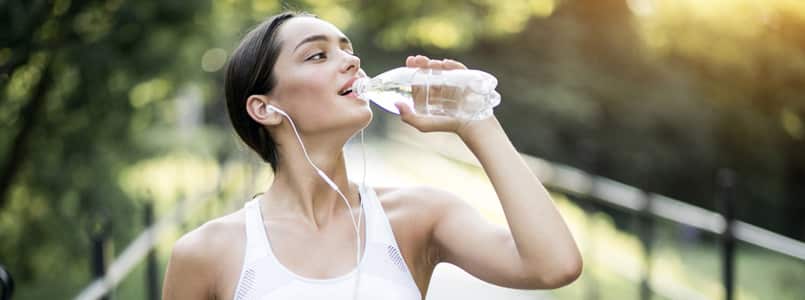 Young woman sipping on water during a run around the park