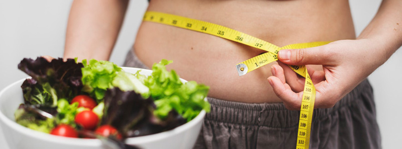person measuring their waist and holding a salad