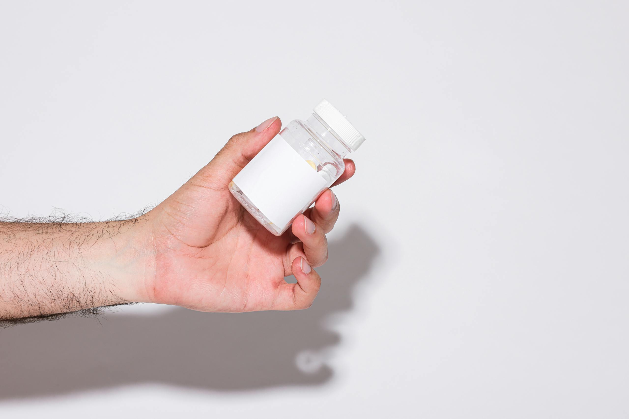 Close-up of a hand holding a small transparent plastic bottle against a bright white background.